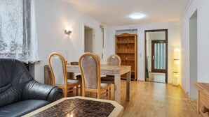 A living room with a leather sofa, a wooden dining table with chairs, a bookshelf, and a door leading to another room. - Apartment 'Buchholz I D N' with Private Terrace, Shared Garden and Wi-Fi (Buchholz in der Nordheide)