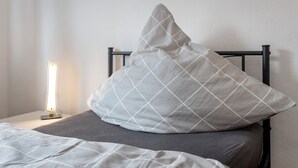 A bed with a pillow, a bedside table with a lamp, and a plain wall. - Apartment 'Buchholz I D N' with Private Terrace, Shared Garden and Wi-Fi (Buchholz in der Nordheide)