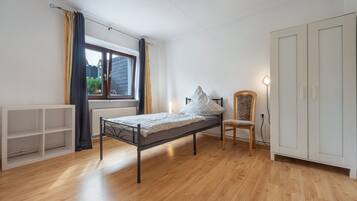 A bedroom with a single bed, a chair, a wardrobe, and a window with curtains.