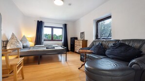 A room with a bed, a wooden chair, a leather couch, a small wooden table, and a window with curtains. - Apartment 'Buchholz I D N' with Private Terrace, Shared Garden and Wi-Fi (Buchholz in der Nordheide)