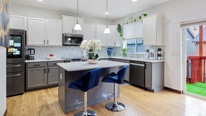 A modern kitchen with white cabinets, stainless steel appliances, and a central island with bar stools. - Sunrise Villa: Solar panels, updated (Bothell)