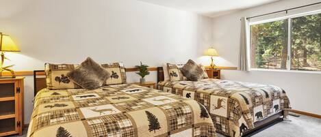 A bedroom with two beds, each with a quilted bedspread featuring animal prints, flanked by bedside tables with lamps.