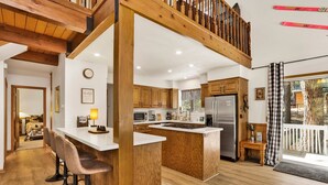 A modern kitchen with wooden cabinets, a large island, bar stools, and a view of the outdoors.