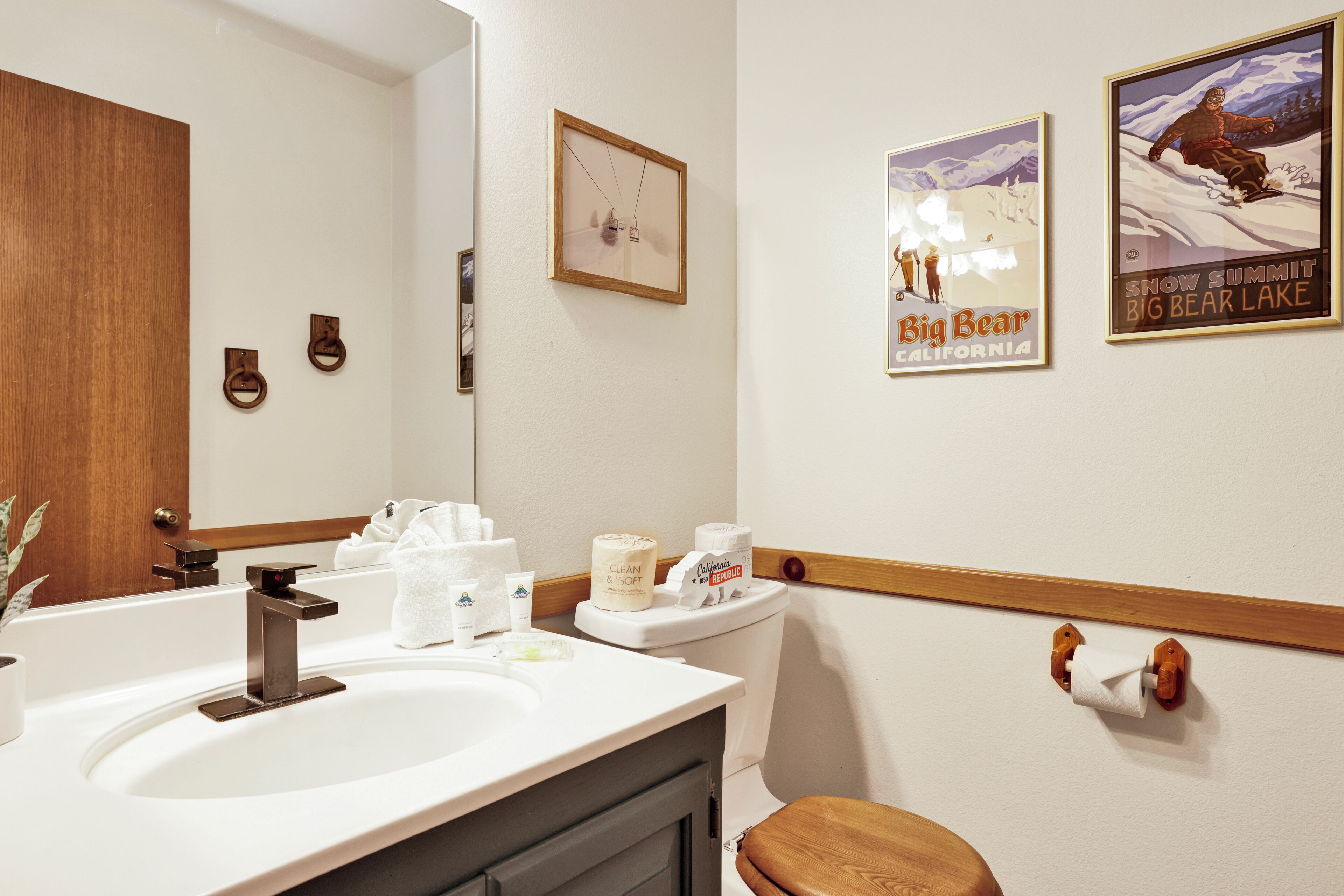 A bathroom with a sink, toilet, and wooden vanity. There are two framed posters on the wall and a mirror above the sink.