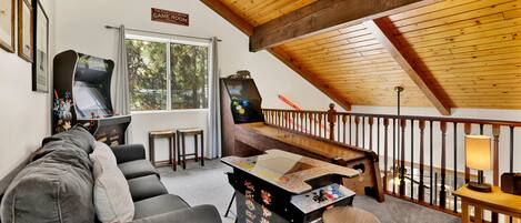 A cozy room with a sloped ceiling, a gaming area with a table and chairs, a couch, and a view of the outdoors through a window.