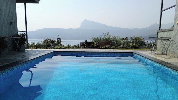 A swimming pool with clear blue water, surrounded by a concrete deck and a wooden bench. - Jumbo Paradise (Mawal)