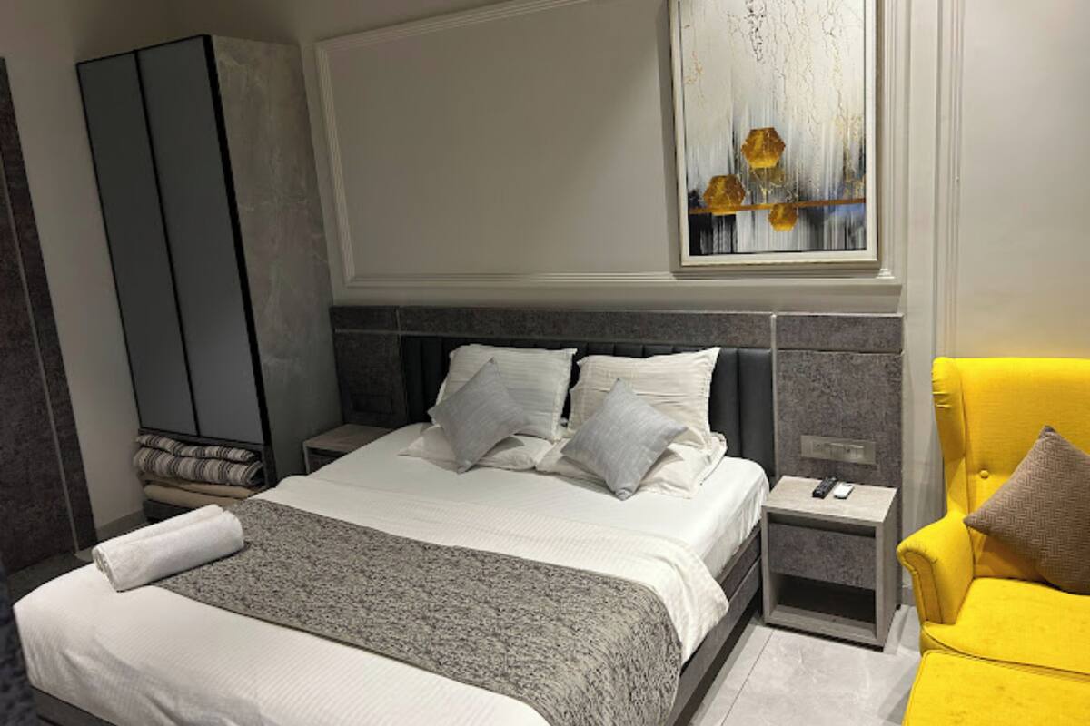 A modern hotel room with a large bed, a nightstand, a chair, and a painting above the bed.