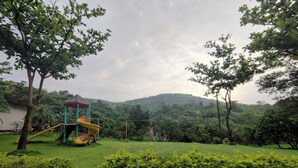 A playground with slides and a climbing structure, surrounded by lush greenery and trees. - Jumbo Paradise (Mawal)