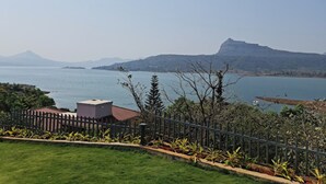 A coastal landscape with a mountain in the background, a fenced garden area, and a body of water. - Jumbo Paradise (Mawal)
