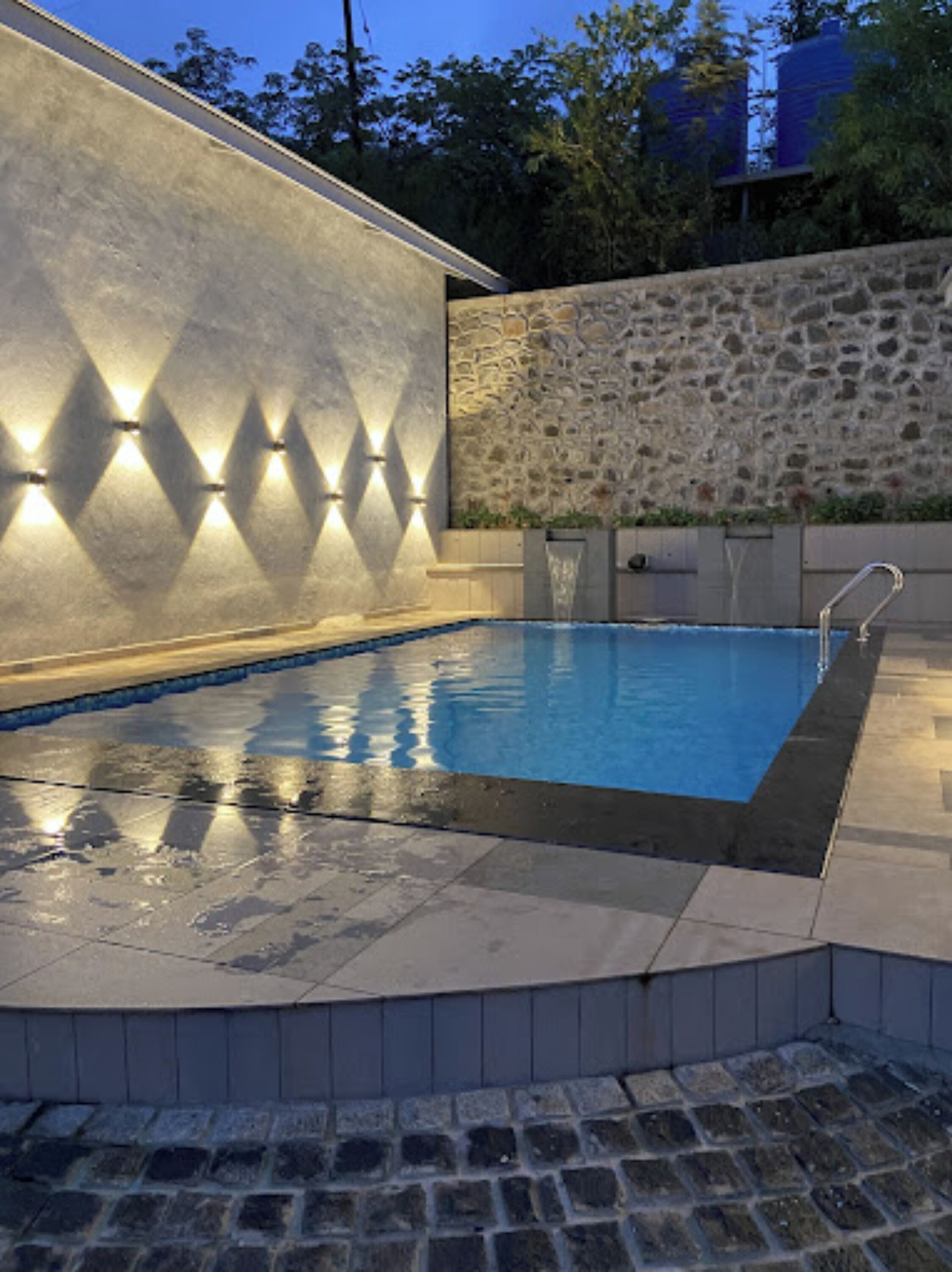 A swimming pool with a stone wall and a modern light fixture.