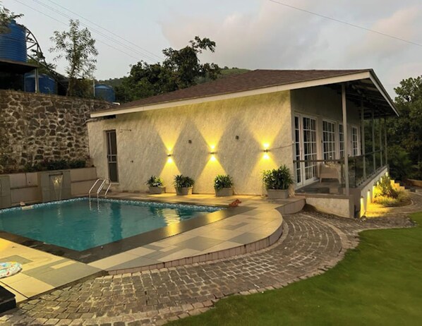 A pool area with a stone wall, a covered patio, and a house with a stone facade and a glass balcony.