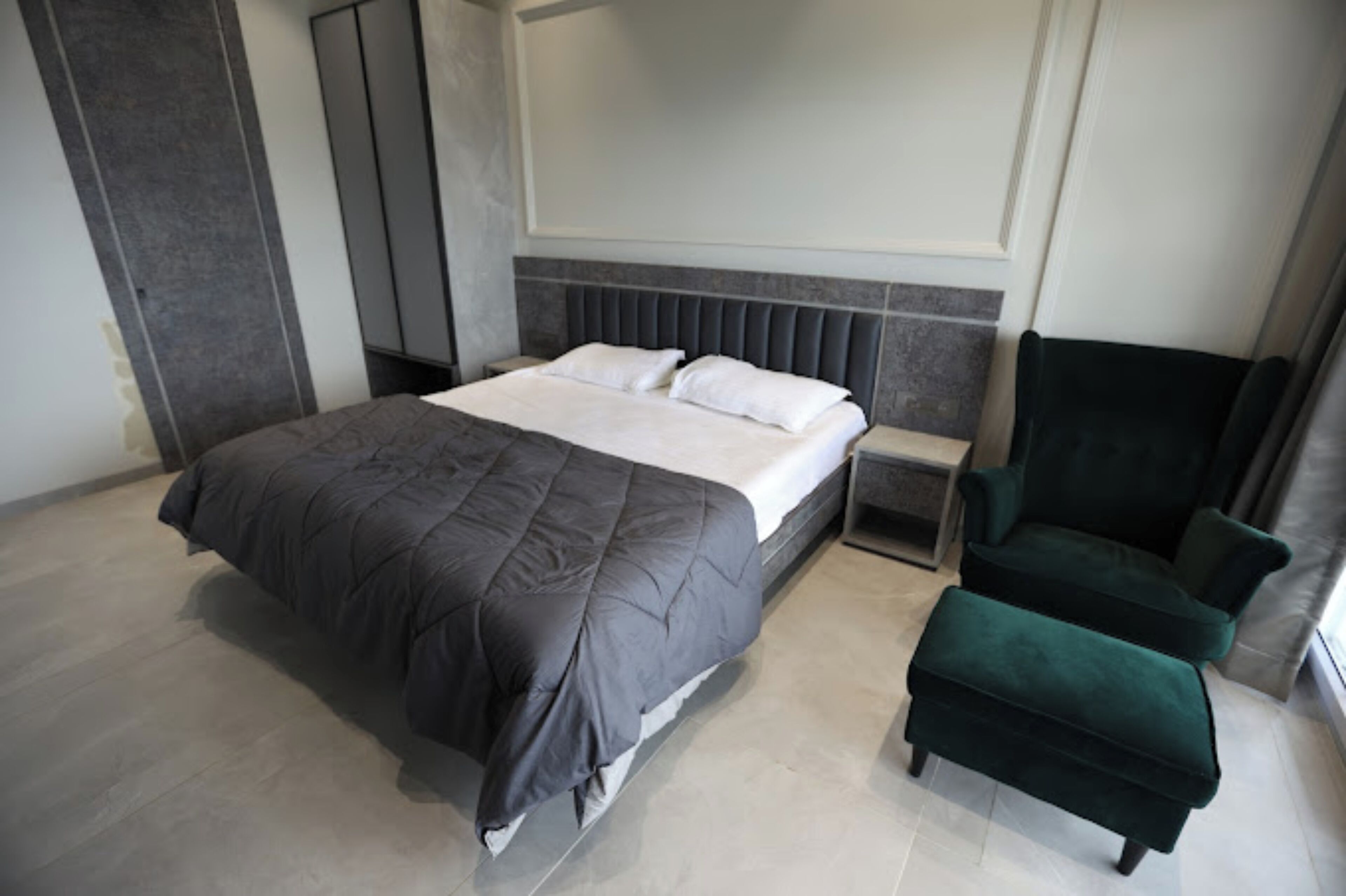 Een moderne slaapkamer met een groot bed, een nachtkastje, een groene fauteuil en een kleine tafel.