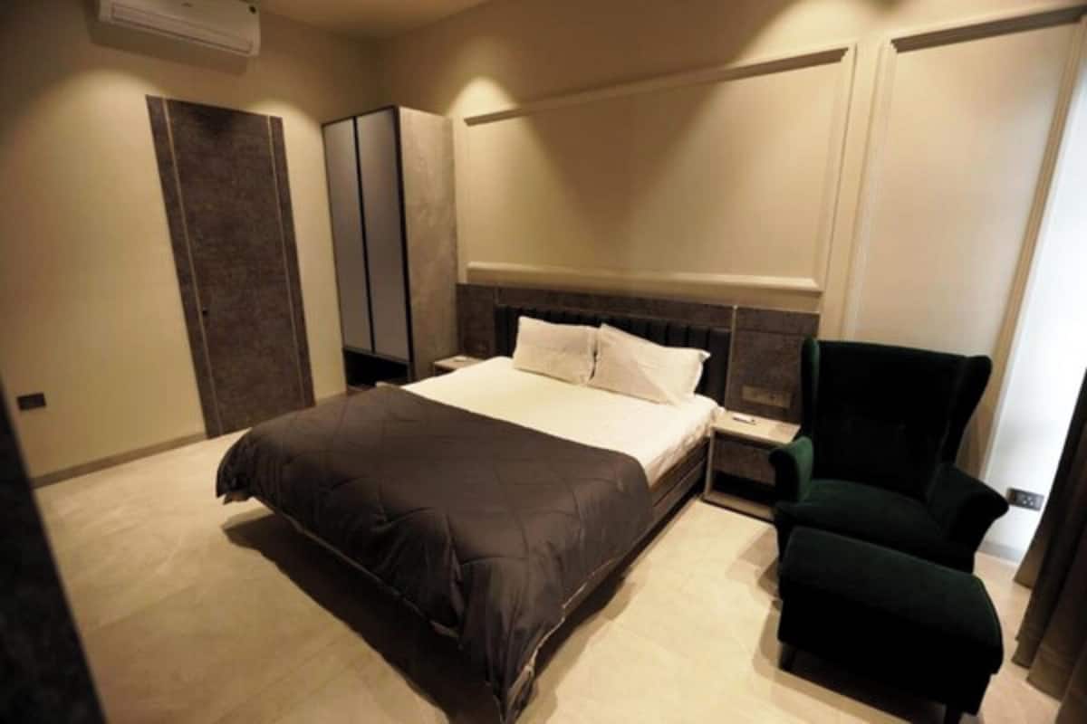 A modern hotel room with a large bed, a nightstand, a green armchair, and a wardrobe.