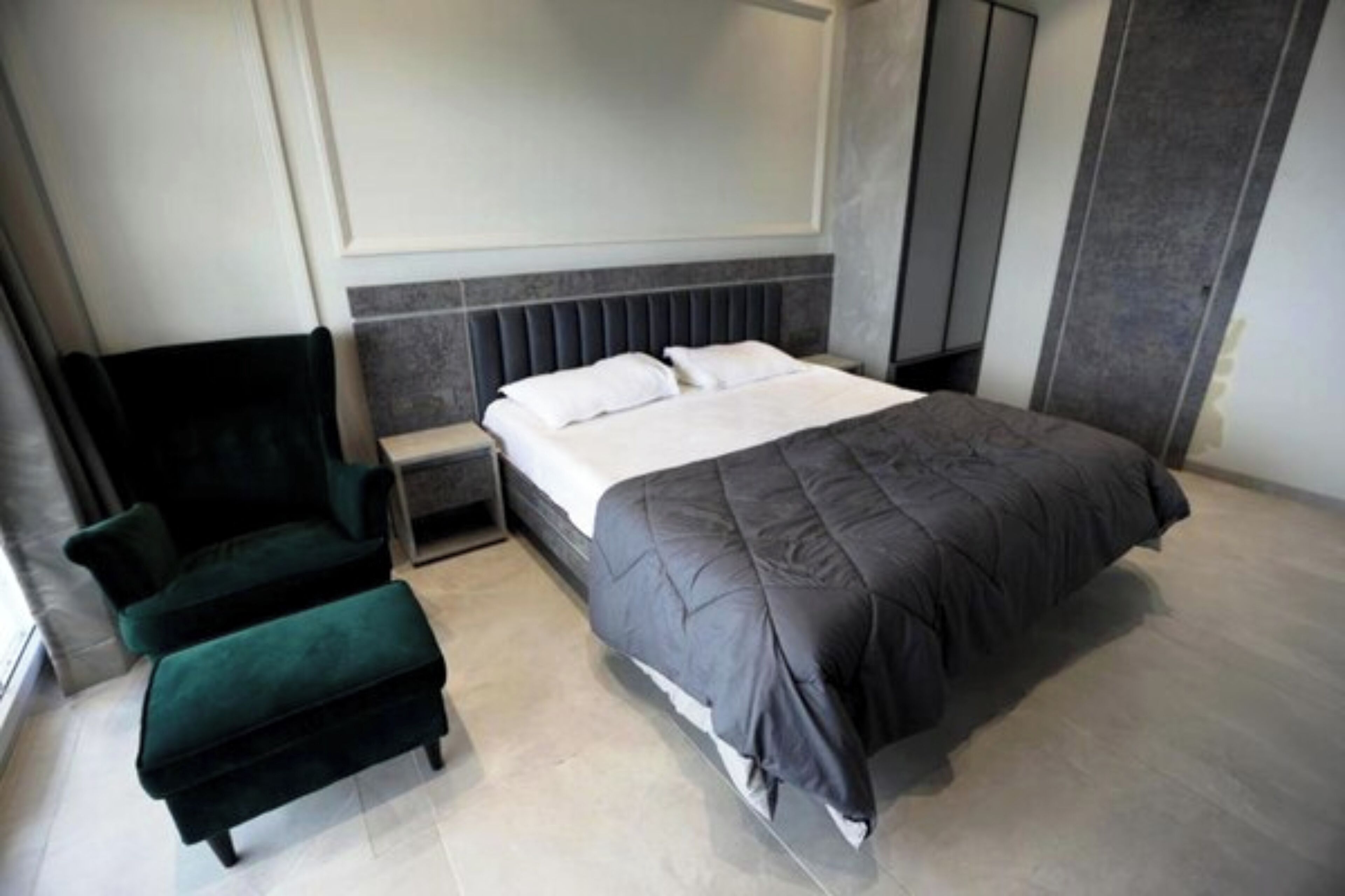 Une chambre moderne avec un grand lit, un fauteuil vert foncé et une table de chevet.