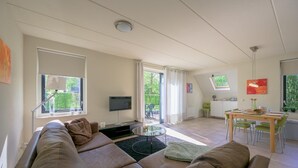 A modern living room with a sofa, a TV, and a dining area with a table and chairs. - Bungalow in Sondel near Slotermeer Lake (Sondel)