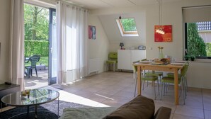 A spacious living area with a glass table, a sofa, and a dining table with chairs. There is a sliding glass door leading to a patio with outdoor furniture. - Bungalow in Sondel near Slotermeer Lake (Sondel)