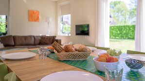 A dining area with a table set for breakfast, including croissants, fruits, and bowls. - Bungalow in Sondel near Slotermeer Lake (Sondel)