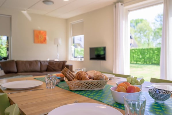 A dining area with a table set for breakfast, including croissants, fruits, and bowls.