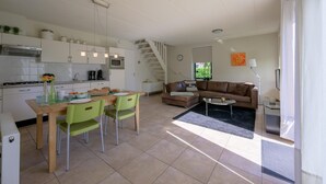 A modern kitchen with white cabinets, a dining area with green chairs, a brown leather sofa, and a staircase leading to another level. - Bungalow in Sondel near Slotermeer Lake (Sondel)