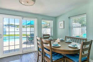 A dining area with a round table, chairs, and a view of a swimming pool through large windows. - Brand New Heated Pool, Hot Tub, Short Walk to Beach, Fenced Yard, Updated Home, $300 in Free Tickets (St. Augustine)