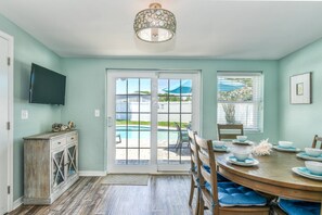 A dining area with a pool view, a television mounted on the wall, and a decorative ceiling light.