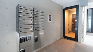 A modern elevator with numbered buttons and a digital control panel, located in a hallway with a tiled floor and a door leading to a room. - Fuente Nishi Sugamo by Tranova (Tokyo)