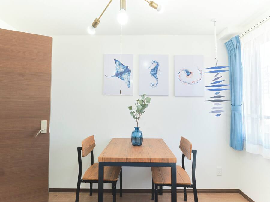 A dining area with a wooden table, four chairs, a vase with greenery, and three wall-mounted artworks.