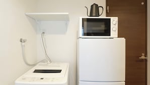Eine kompakte Küchenzeile mit Mikrowelle, kleinem Kühlschrank und Durchlauferhitzer.