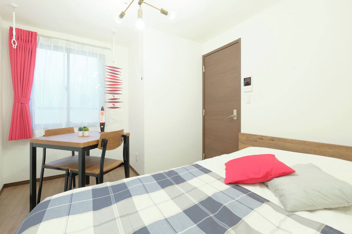 A bedroom with a bed, a wooden headboard, a bedside table with a lamp, a chair, and a window with curtains.