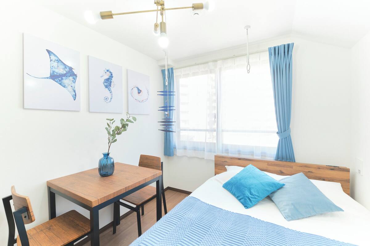 A bedroom with a bed, a wooden table, chairs, and artwork on the wall.