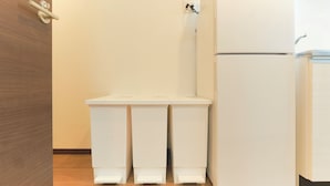 A kitchen with a white refrigerator, two trash bins, and a wooden door. - Fuente Nishi Sugamo by Tranova (Tokyo)