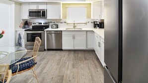 A modern kitchen with white cabinets, stainless steel appliances, a glass dining table, and a wooden floor. - The Blooming Sanctuary - 3br with pool and EV-Charger (Rotonda West)