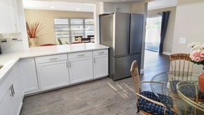 A modern kitchen with white cabinets, a stainless steel refrigerator, and a glass dining table. - The Blooming Sanctuary - 3br with pool and EV-Charger (Rotonda West)