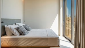 Ein modernes Schlafzimmer mit einem großen Bett, einer Kopfteil und Blick ins Freie durch ein großes Fenster.