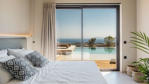 Ein Schlafzimmer mit einem großen Bett, Blick auf Pool und Landschaft sowie einer Schiebetür.