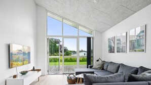 Un salon moderne avec un canapé d’angle gris, une console blanche et une grande porte-fenêtre coulissante donnant sur un balcon.