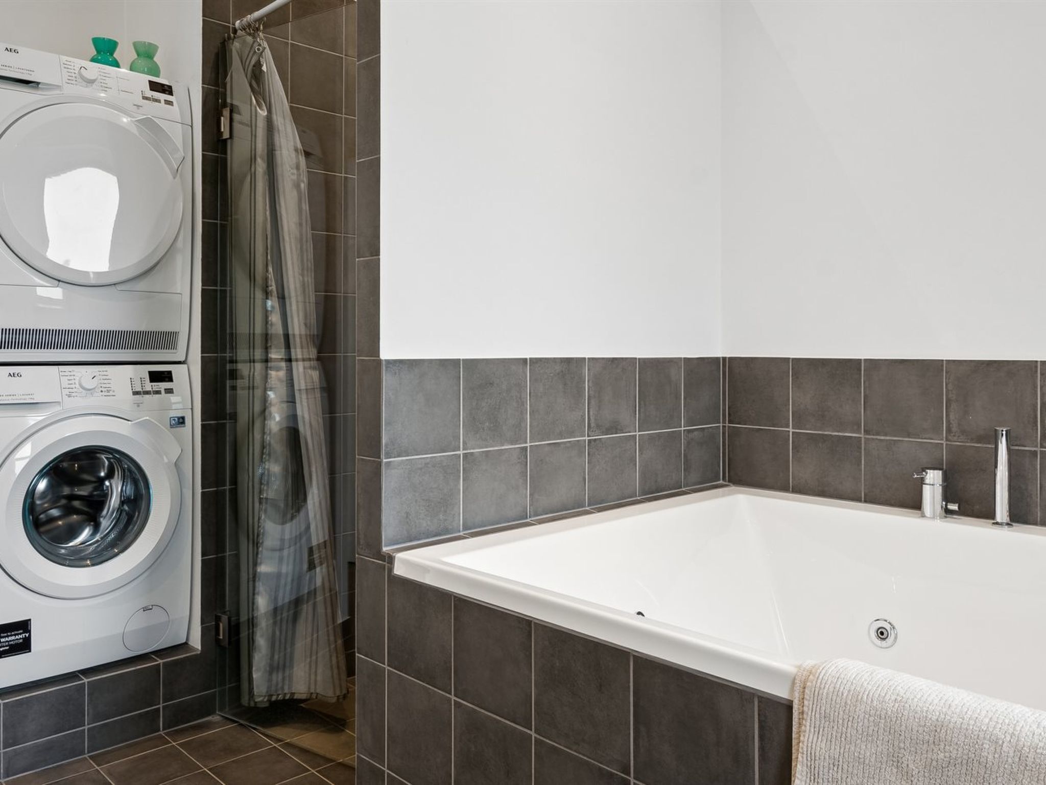 Ein modernes Badezimmer mit einer Frontlader-Waschmaschine, einer Badewanne und grauen Fliesen.