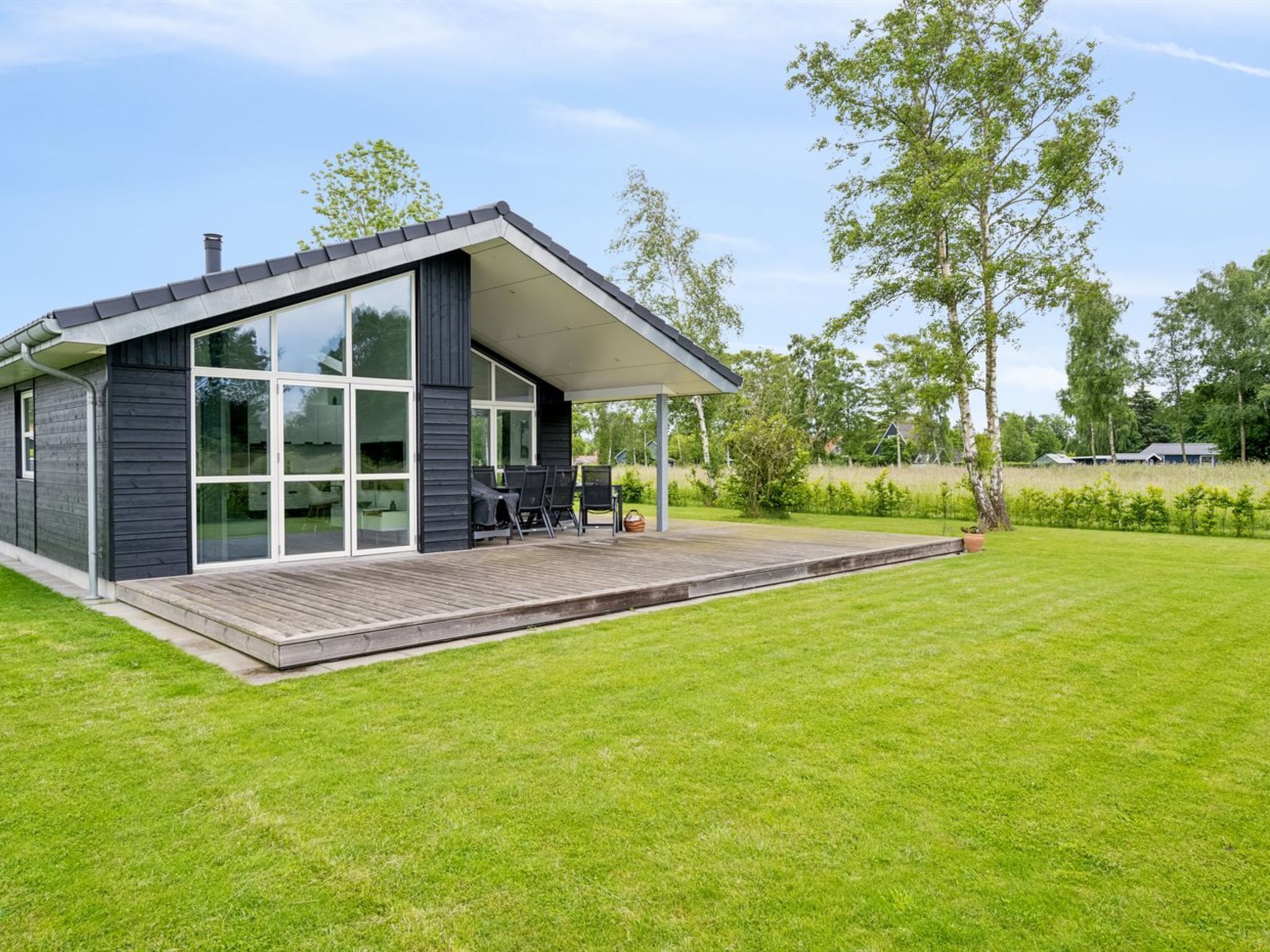 A modern house with a large glass window, a wooden deck, and a grassy yard.
