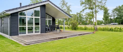 A modern house with a large glass window, a wooden deck, and a grassy yard.