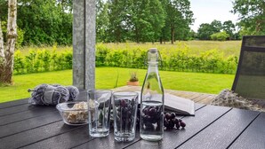 Une table avec une bouteille, des verres, des raisins et un bol de nourriture, le tout installé dans un jardin.