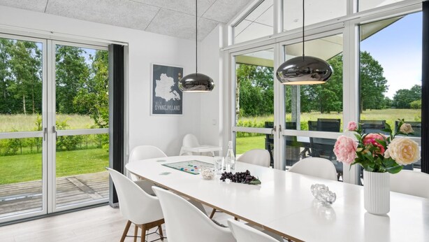 Un espace de restauration moderne, doté d’une grande table, de chaises blanches et offrant une vue sur un paysage verdoyant grâce à de larges fenêtres.