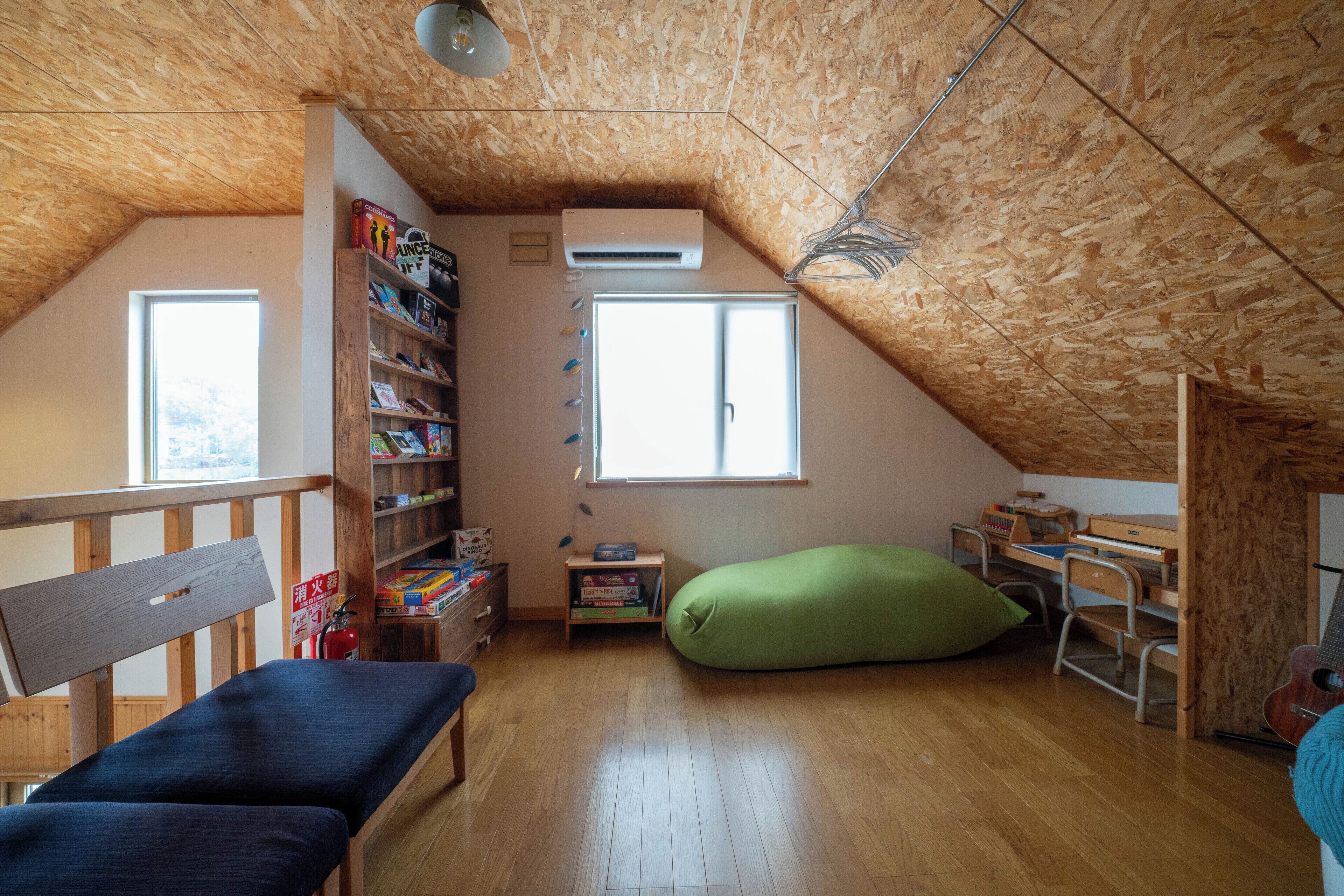 A cozy attic bedroom with a sloped wooden ceiling, a bunk bed, a desk, a green bean bag, and a bookshelf filled with books and games.