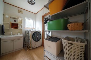 A laundry room with a washing machine, a sink, and shelves with baskets and containers. - RONIN LODGE (Furano)