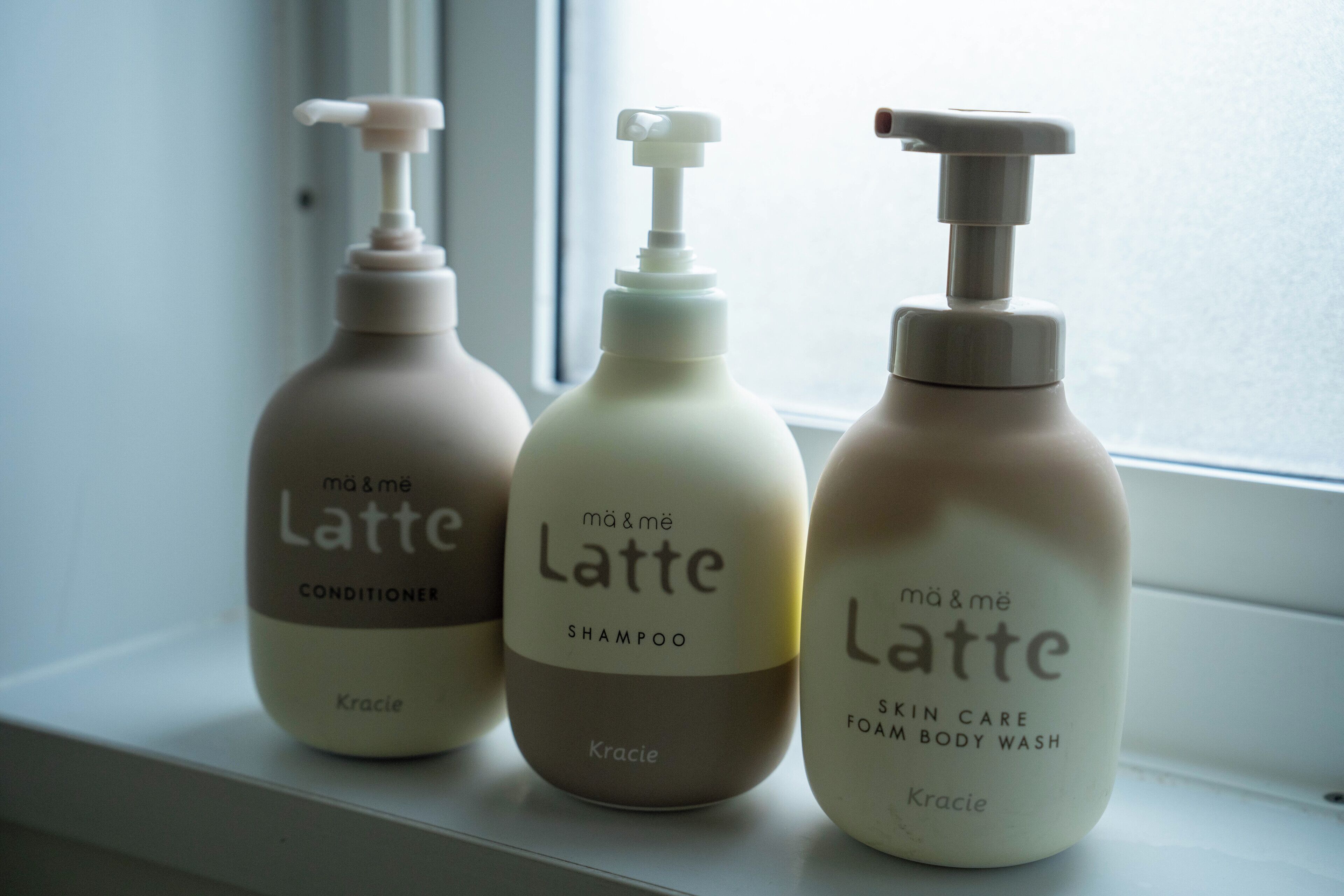 Tre flasker 'mā & mē Latte' hudplejeprodukter står på et vindueskar.