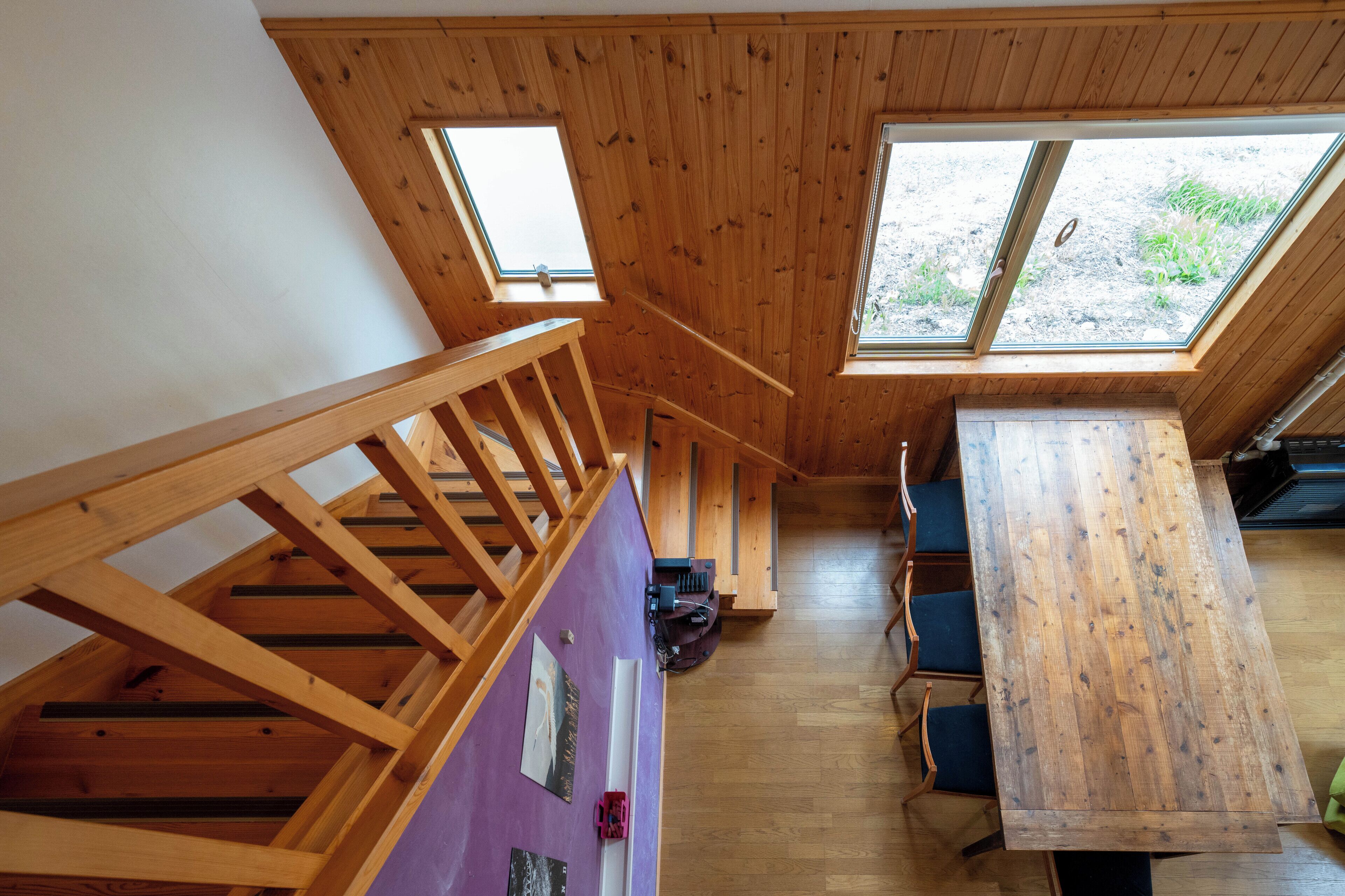 A wooden interior with a staircase, a dining area, and large windows.
