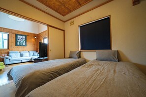 A bedroom with two beds, a television, and a sofa in a wooden-paneled room. - RONIN LODGE (Furano)