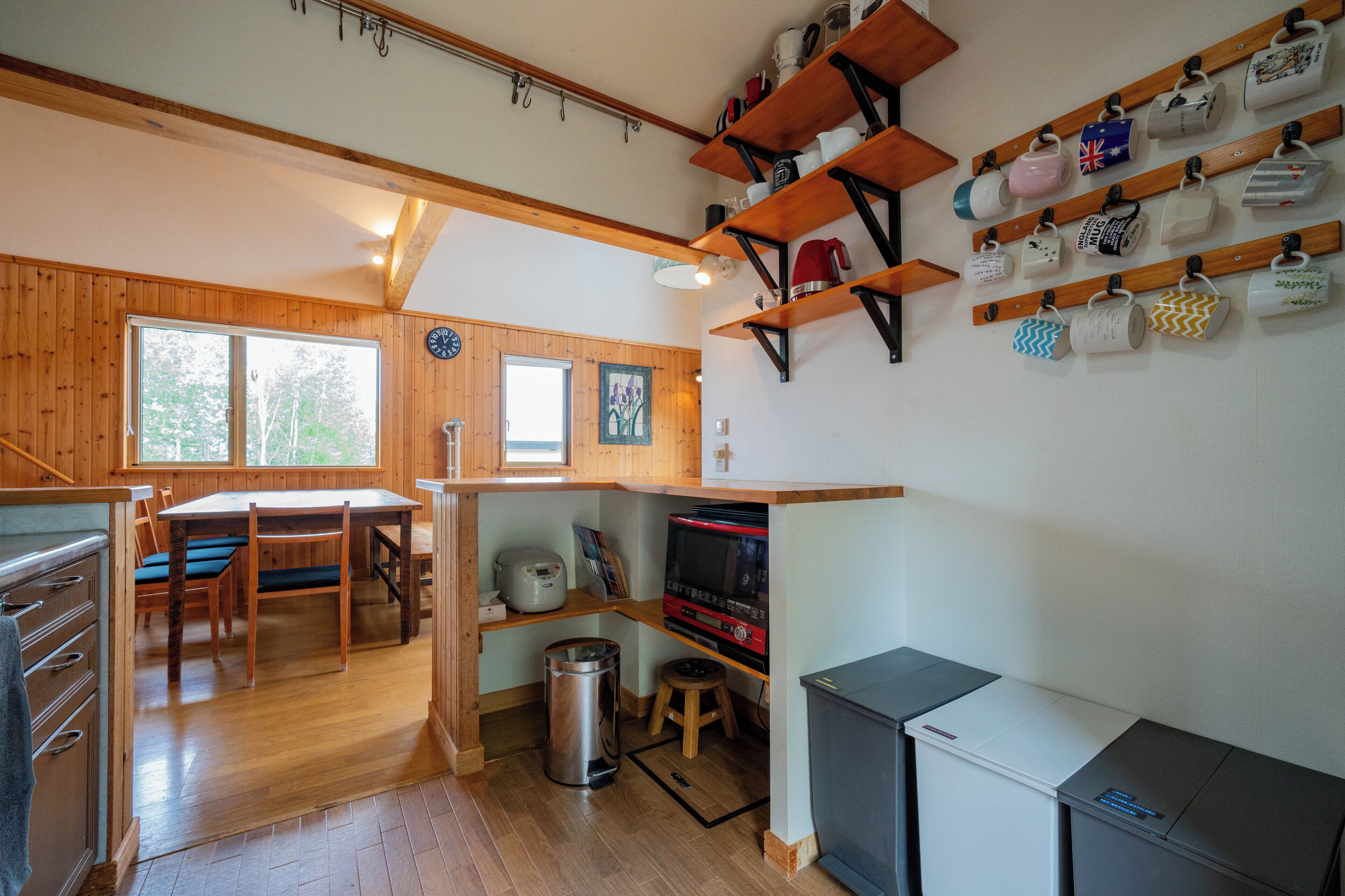 A wooden cabin interior with a dining area, kitchen, and shelves with mugs.