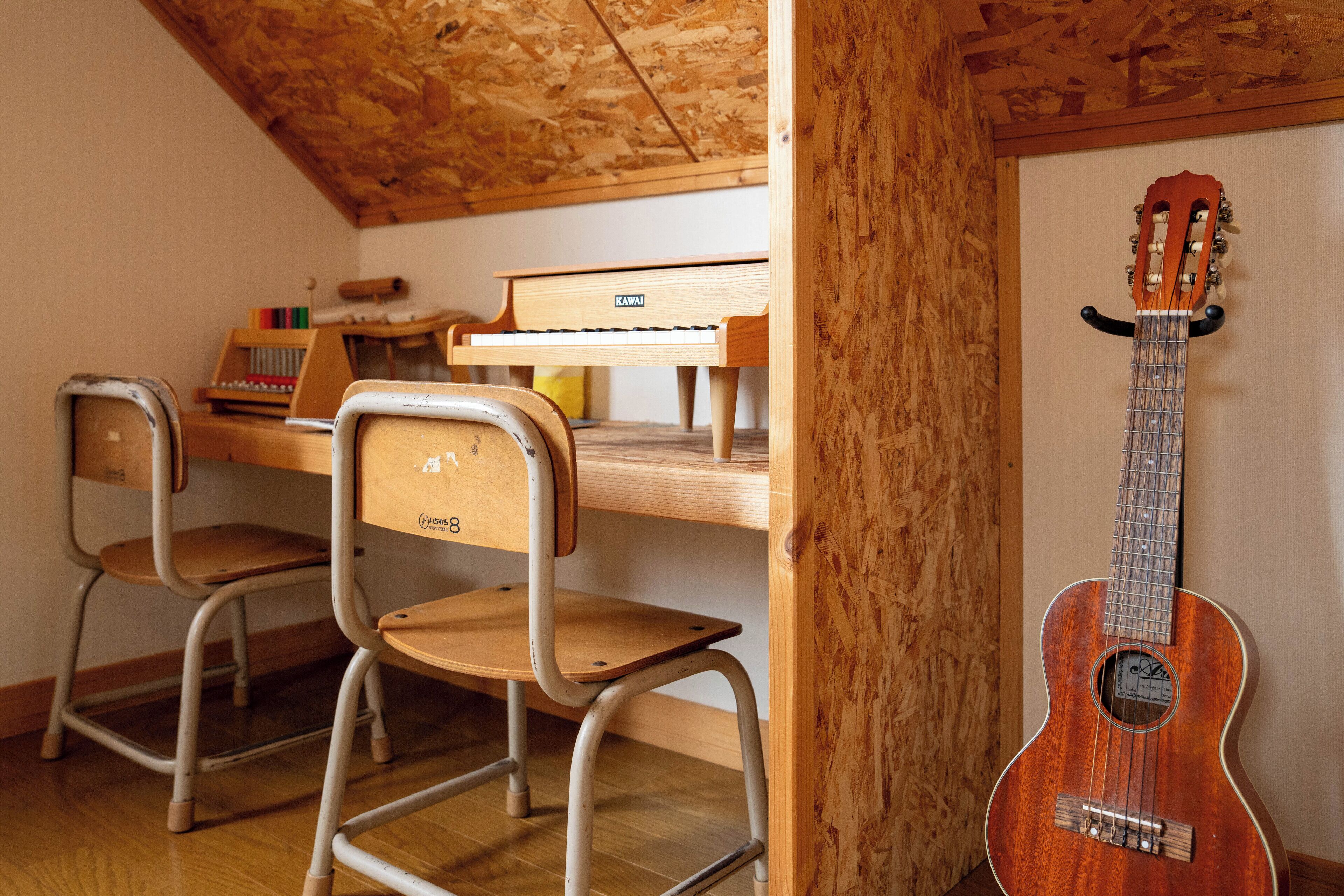 A room with a wooden ceiling, a piano, two metal chairs, and a guitar leaning against the wall.
