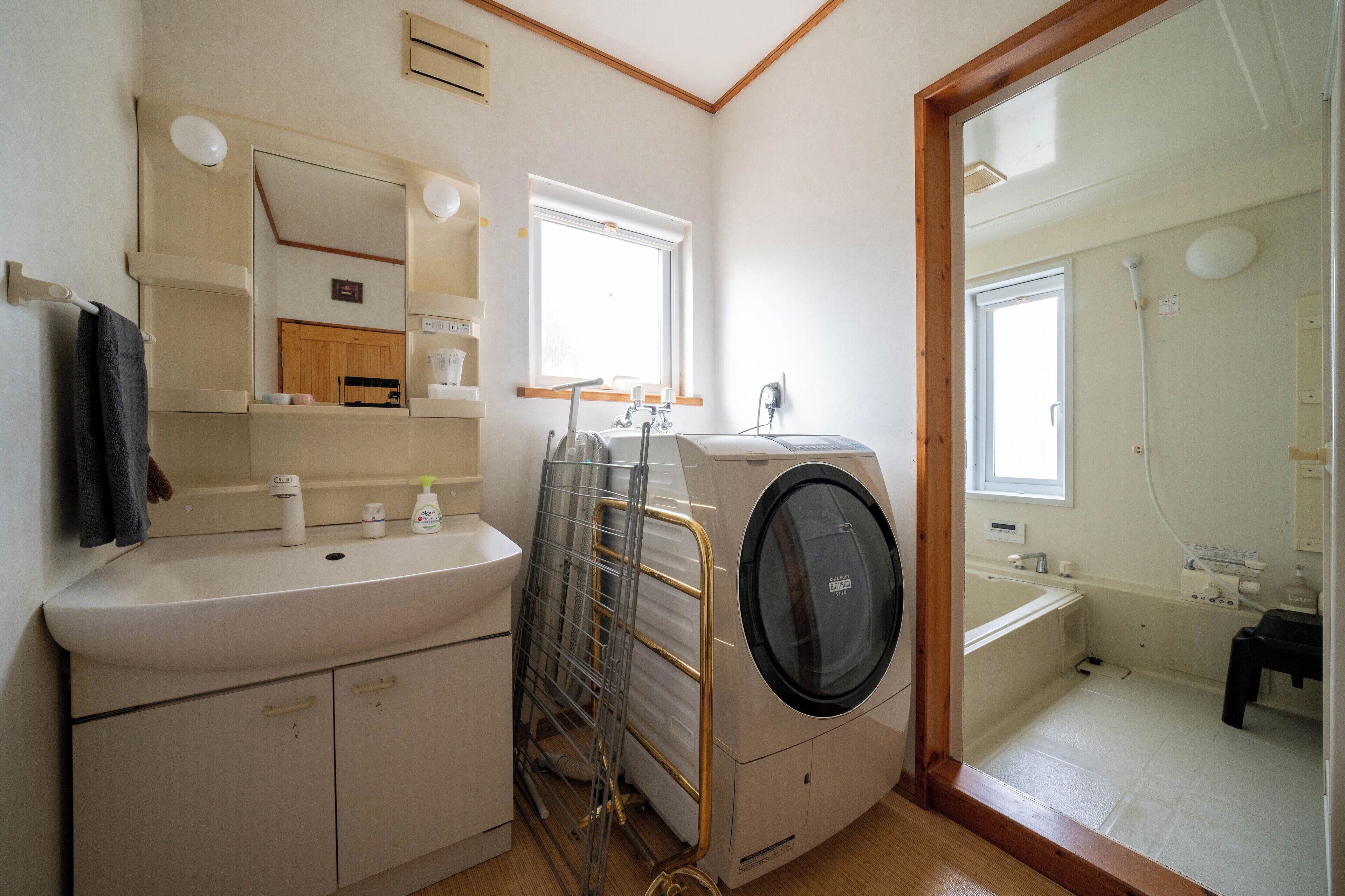 A compact bathroom with a sink, mirror, window, and a built-in washing machine.