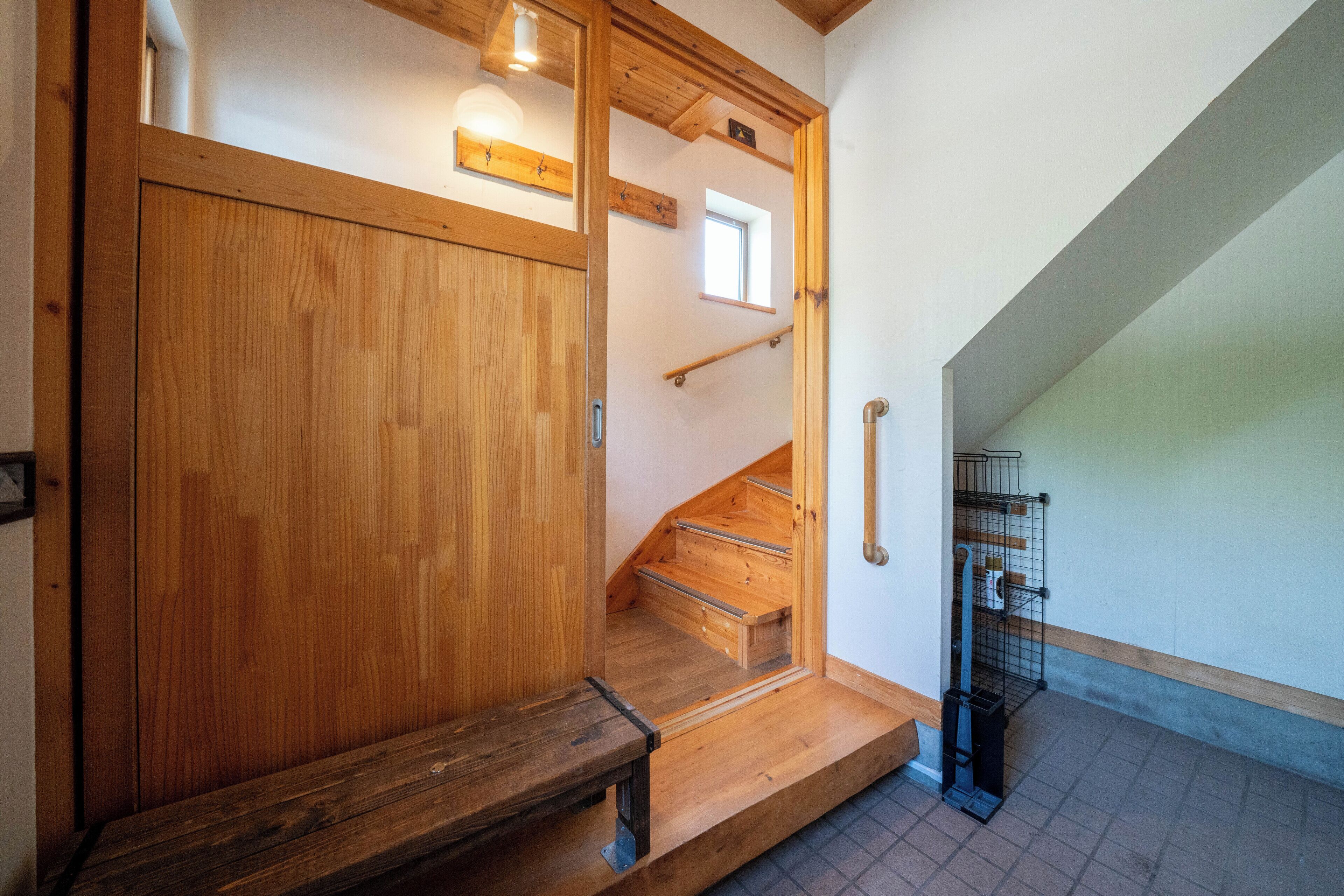 A wooden staircase with a handrail, a wooden bench, and a metal rack with items on the floor.